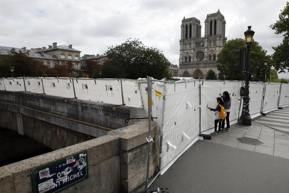 Tourists peer through protection panels securing a perimeter around the Notre Dame Cathedral ahead of the start of a massive lead decontamination in Paris, Thursday, Aug. 15, 2019. (AP Photo/Francois Mori)