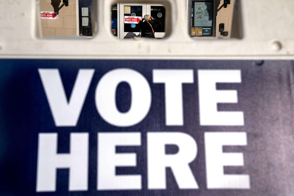 FILE - A woman is seen through a "vote here" sign, as she enters a polling site to vote in the midterm elections, Nov. 8, 2022, in Washington. Officials at Meta say they have found and disabled a network of thousands of fake Facebook accounts linked to China that were used to spread partisan content in the U.S. The accounts disclosed on Nov. 30, 2023, were designed to look like they were run by everyday Americans. (AP Photo/Jacquelyn Martin, File)