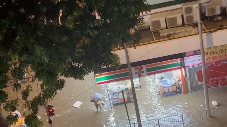 A person holding an umbrella walks a flooded road amid torrential rain in Hong Kong.