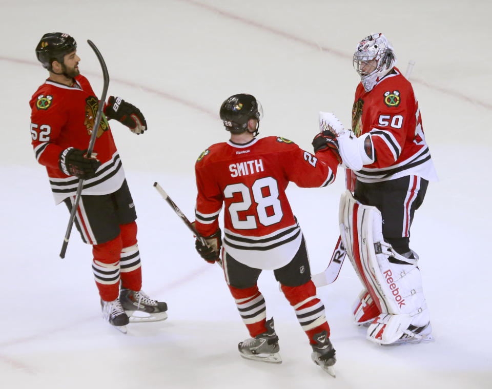 Chicago Blackhawks goalie Corey Crawford (50) celebrates with Brandon Bollig (52) and Ben Smith after the Blackhawks' 2-0 win over the St. Louis Blues in Game 3 of a first-round NHL hockey Stanley Cup playoff series game Monday, April 21, 2014, in Chicago. (AP Photo/Charles Rex Arbogast)