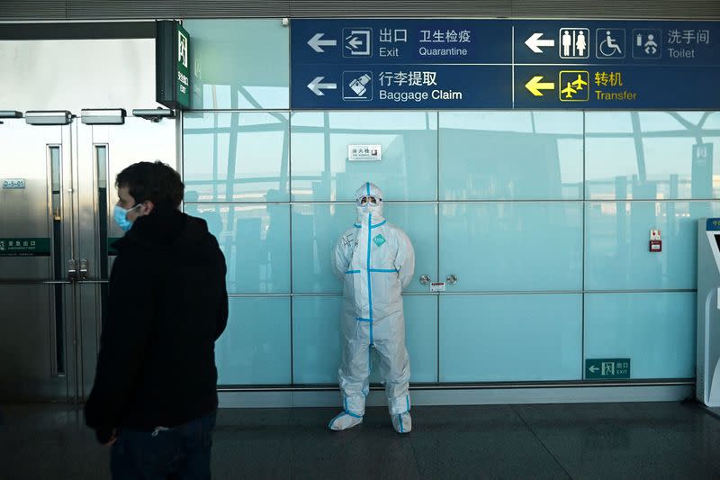 A staff member wearing PPE waits as passengers arrive at the Beijing Capital International Airport ahead of the Beijing 2022 Winter Olympics in Beijing