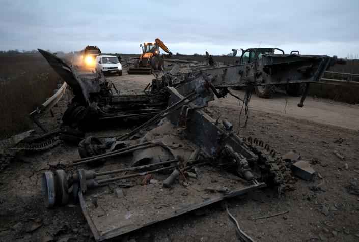 Cars and trucks drive past a destroyed military vehicle on the road in Ukraine&#39;s Kherson region.