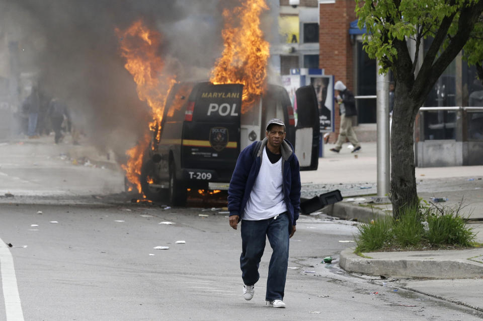 A man walks past a burning police vehicle, Monday, April 27, 2015, during unrest following the funeral of Freddie Gray in Baltimore. Gray died from spinal injuries about a week after he was arrested and transported in a Baltimore Police Department van. (AP Photo/Patrick Semansky)