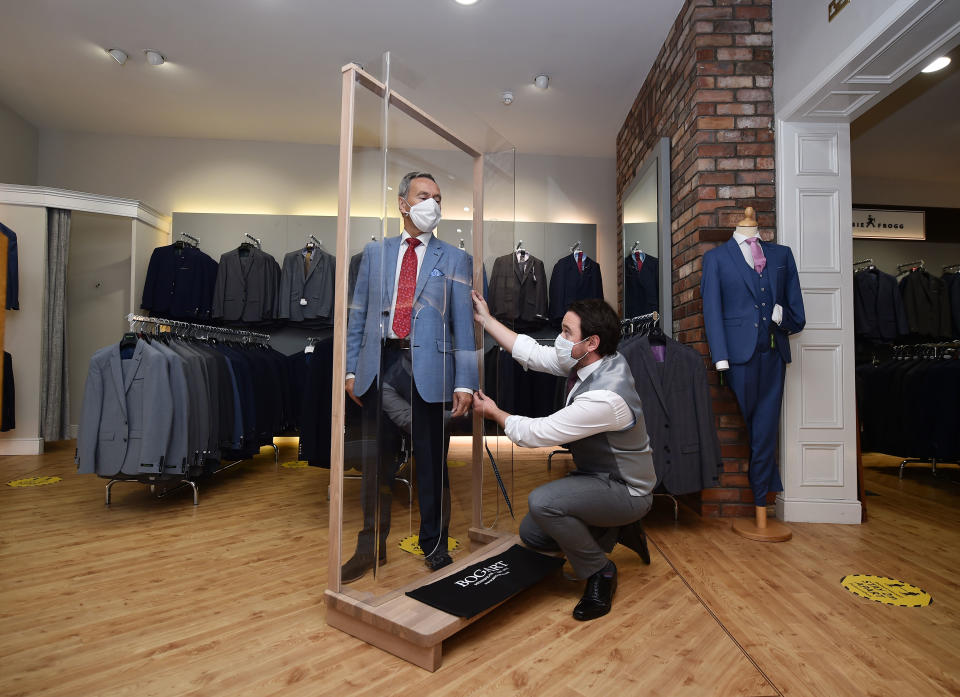 BELFAST, NORTHERN IRELAND - JUNE 12: Tailor Gary Keenan (R) of Bogart Menswear measures up a suit using a customer pod designed to keep customers safe from Covid-19 after their store reopened for business on June 12, 2020 in Belfast, Northern Ireland. After being shuttered for months to curb the spread of Covid-19, retailers here reopened with social distancing measures, a few days ahead of when similar businesses can reopen in England. (Photo by Charles McQuillan/Getty Images)