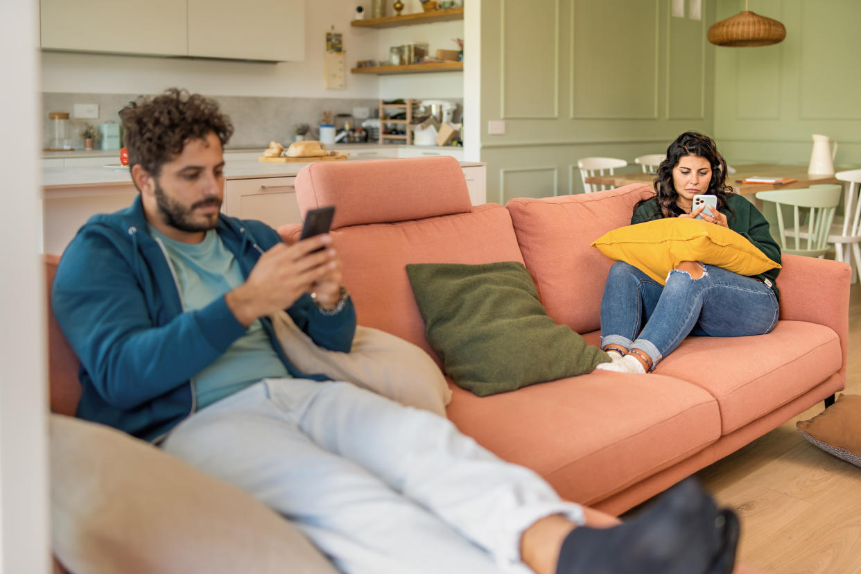 Young married couple using smart phone ignoring each other addicted digital detox to the internet and social network - man and woman phubbing in the living room - family people loneliness and technology lifestyle concept