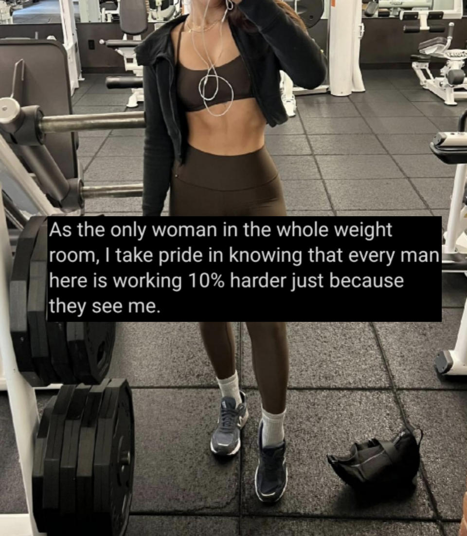 A person is taking a mirror selfie in a gym. They are wearing a sports bra, high-waisted leggings, a zip-up jacket, and athletic shoes. Their face is not visible