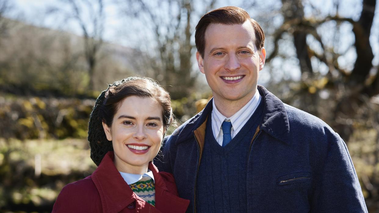  Rachel Shenton in a red coat as Helen and Nicholas Ralph in a blue coat as James stand together outdoors in All Creatures Great and Small. 