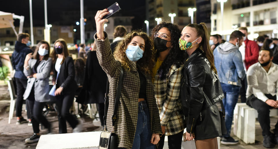 Three women pose for a selfie in a busy Italian street.