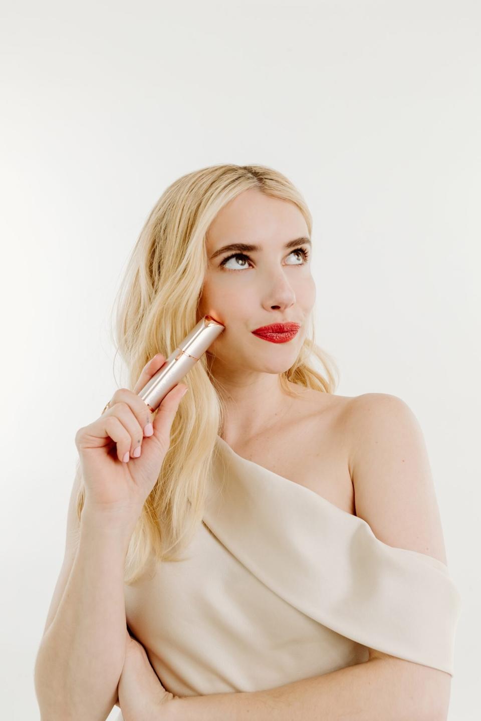 Emma Roberts with bright red lipstick holding lipstick