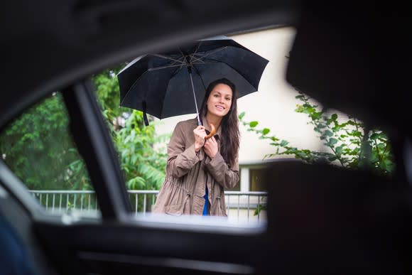 Woman holding a black umbrella peeks into a car window in front of her to check if it's her Uber ride