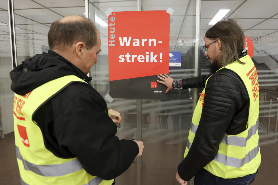 Union representatives stick a poster reading "Warning strike!" on a glass door at Hamburg Airport, Sunday, March 26, 2023, in Hamburg, Germany. The trade union Verdi and the Railway and Transport Union (EVG) have called for a nationwide warning strike in the transport sector on Monday. (Bodo Marks/dpa via AP)