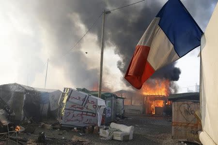 A French flag flies from a makeshift shelter as others burn in the "Jungle" on the third day of the evacuation and transfer of migrants to reception centers in France, as part of the dismantlement of the camp in Calais, France, October 26, 2016. REUTERS/Pascal Rossignol