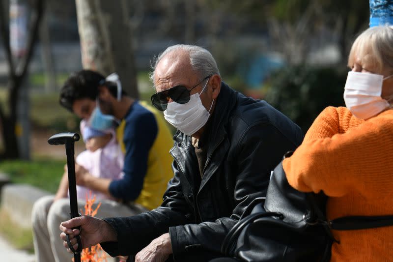 People wearing protective face masks sit outside the AHEPA hospital, where the first confirmed coronavirus case is being treated, in Thessaloniki