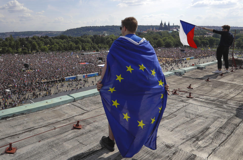 A man wrapped in a European Union flag watches protesters gather in Prague, Czech Republic, Sunday, June 23, 2019. Protesters are on calling on Czech Prime Minister Andrej Babis to step down over fraud allegations and subsidies paid to his former companies. (AP Photo/Petr David Josek)