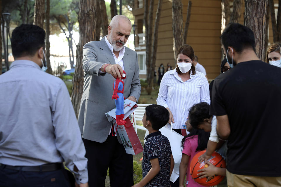 Albanian Prime Minister Edi Rama offers a gift to a boy during his visit at a resort which is accommodated Afghan refugees in Golem, 45 kilometres (30 miles) west of the capital Tirana, Friday, Aug. 27, 2021. Albania on Friday housed its first group of Afghan evacuees who made it out of their country despite days of chaos near the Kabul airport, including an attack claimed by the Islamic State group. (AP Photo/Franc Zhurda)