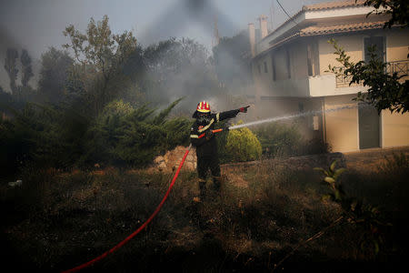 A firefighter gestures as he extinguishes a fire threatening a house during a wildfire near the village of Kapandriti, north of Athens, Greece, August 15, 2017. REUTERS/Alkis Konstantinidis