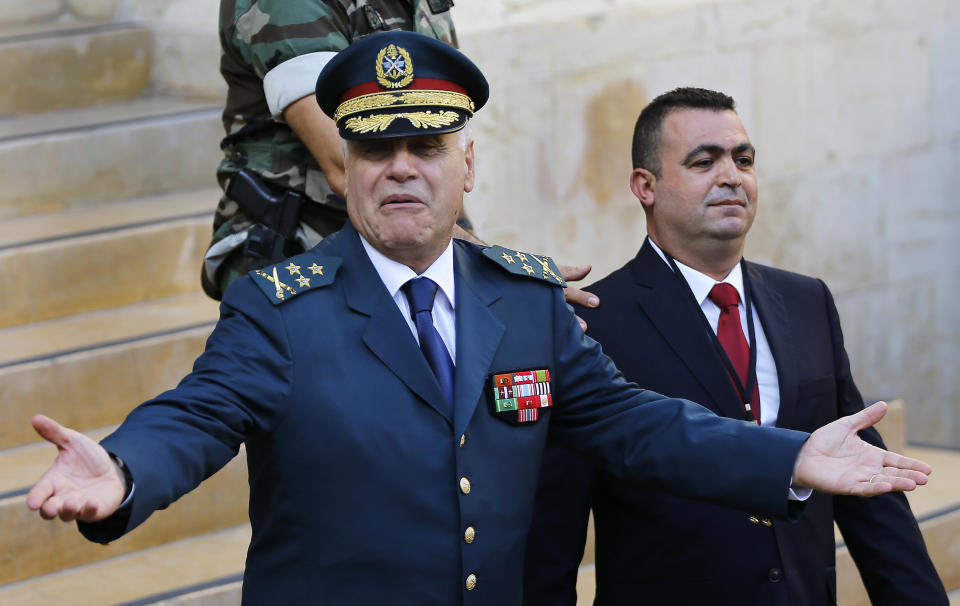 File - In this Oct. 31, 2016 file photo, Lebanese Army Commander Jean Kahwaji, left, reacts as he leaves the parliament building after he attended the session of the presidential elections, in Beirut, Lebanon. Lebanon's former army chief Jean Kahwaji told the lead investigator of last year's massive Beirut port blast on Thursday, Feb. 11, 2021, that he recommended years before the explosion that tons of seized ammonium nitrate stored there be sold privately or sent back to importer because the military had no use for them. (AP Photo/Hussein Malla)