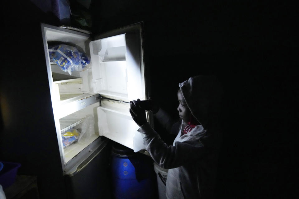 Jeffrey Carlos' daughter Tracy uses the light from a mobile phone to look inside their family fridge in Mabvuku on the outskirts of Harare on Wednesday, Aug, 3, 2022. Carlos, a father of three, says he gets about $100 dollars a month from his job as an overnight security guard for a church and the bar next door. Rising prices and a fast-depreciating currency have pushed many Zimbabweans to the brink, reminding people of when the southern African country faced world-record inflation of 5 billion % in 2008.(AP Photo/Tsvangirayi Mukwazhi)