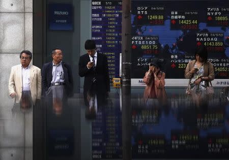 Pedestrians standing in front of an electronic board showing the various countries' stock market indices outside a brokerage are reflected in a polished stone surface, in Tokyo May 13, 2014. REUTERS/Yuya Shino