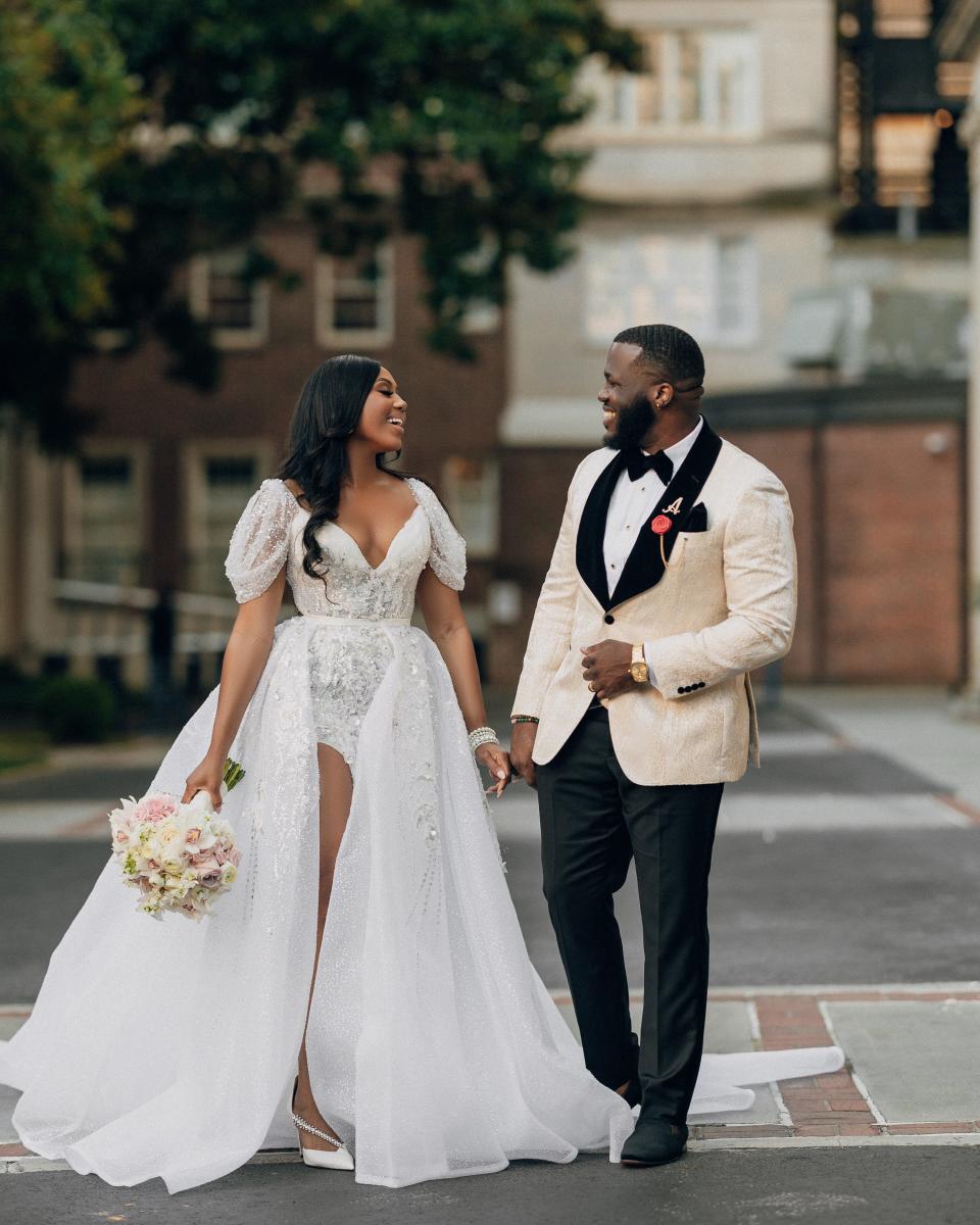 A bride and groom look at each other and smile in the middle of a street.