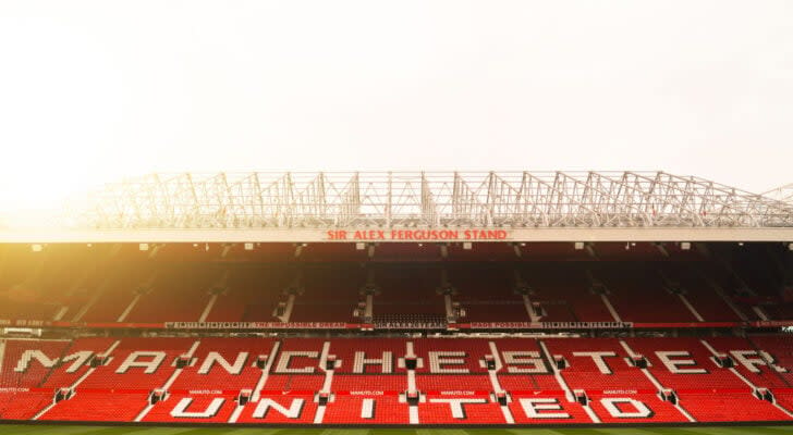 Wide shot photo of Manchester United (MANU) stadium seating at sunset, red seats with white text reading "Manchester United"