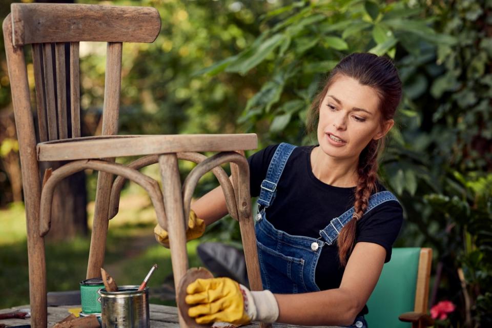 Woman sanding a wooden chair outdoors.