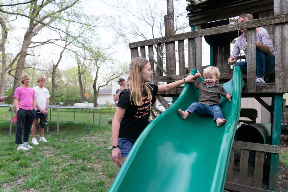 Norah Budge, 12, helps her brother Tate, 1, down a slide in the yard as her mom, Sunny, right, dad Tim, middle, and brothers David and Wesley watch Monday at their home in Shawnee County. Norah, a sixth-grader in the Seaman USD 345 district, is still recovering after a sinus infection moved to her brain early last month.