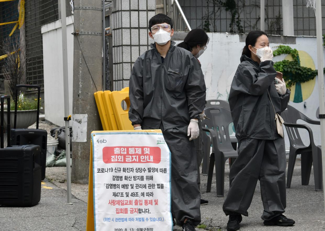 Government officials wearing protective clothing stand at a temporary check point to restrict access to the Sarang Jeil Church in Seoul on August 17, 2020. - Thousands of Protestant church members in Seoul have been asked to quarantine, South Korean authorities said on August 17, as the country battles virus clusters linked to religious groups. A total of 315 cases linked to the Sarang Jeil Church had been confirmed so far, officials said, making it one of the biggest clusters so far, and around 3,400 members of the congregation had been asked to quarantine. (Photo by Jung Yeon-je / AFP) (Photo by JUNG YEON-JE/AFP via Getty Images)