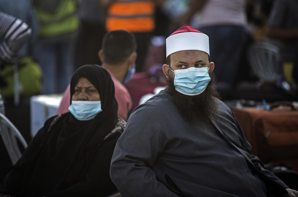 Palestinians wearing face masks sit next to their luggage as they wait to cross to the Rafah border with Egypt, in the southern Gaza Strip, Sunday, Sept. 27, 2020. (AP Photo/Khalil Hamra)