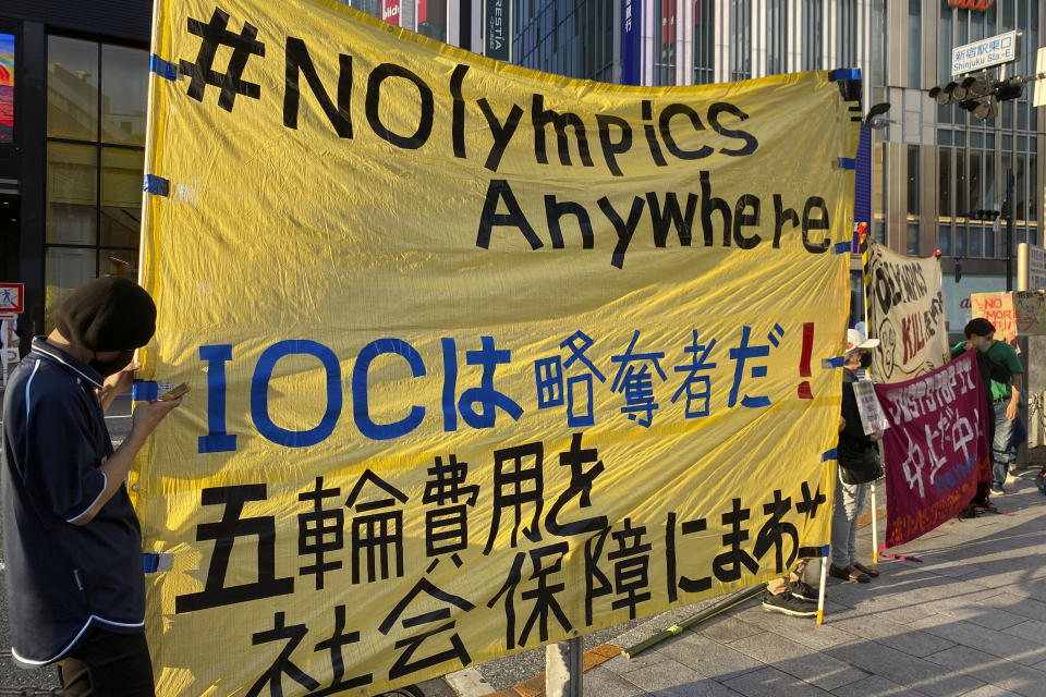 Protesters hold a banner which reads "The IOC is a bunch of thieves. Spend on welfare, not the Games." in Shinjuku district of Tokyo, Japan, Sunday, June 12, 2022. Holding “No Olympics” banners, protesters demanded Japan drop its bid for the 2030 Winter Games Sunday. (AP Photo/Yuri Kageyama)