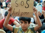 A migrant boy holds a sign reading 'SOS help me' as he sits with other migrants in front of the Keleti (East) railway station in Budapest on September 2, 2015