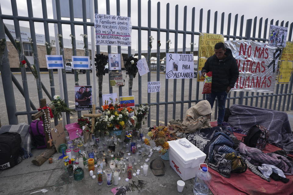 Un altar con velas y fotos cubre la cerca afuera del centro de detención de migrantes que fue el sitio de un incendio mortal, mientras los migrantes se despiertan después de pasar la noche en la acera en Ciudad Juárez, México, el jueves 30 de marzo de 2023. (AP Foto/Fernando Llano)