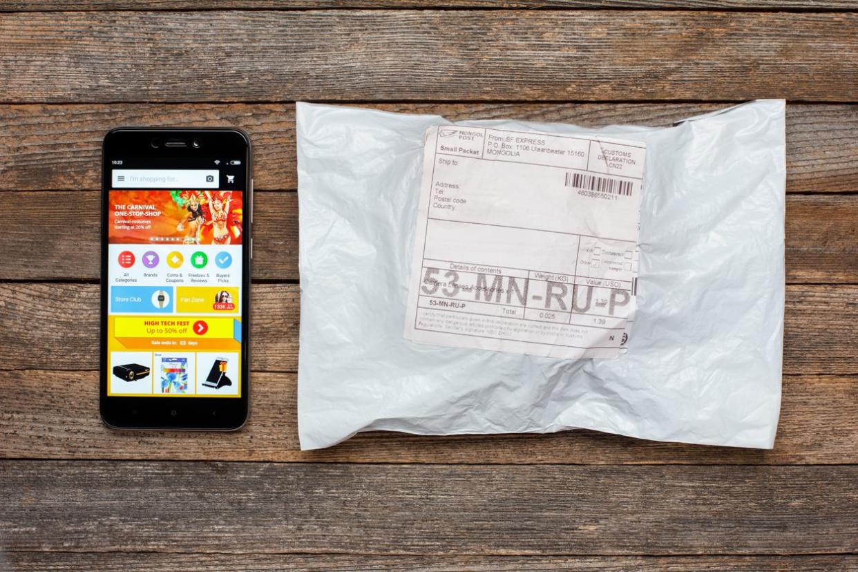 Mobile application of the Chinese online store ali express on the screen of the smartphone xiaomi and package parcel on the wooden table
