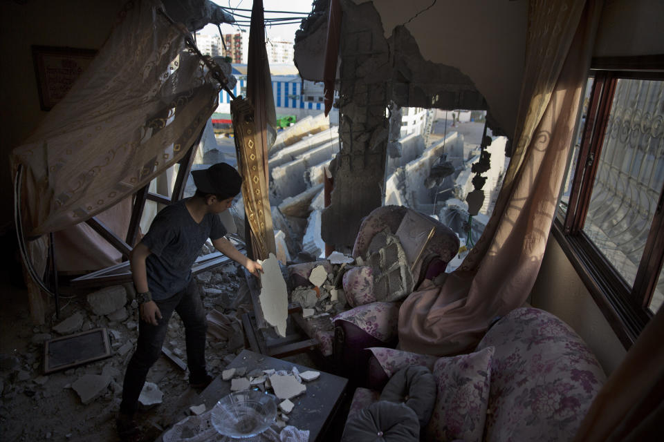 A Palestinian boy cleans a sofa from the rubble of the partial damage on his family house after and Israeli airstrike, Sunday, on a next door multi-story building in Gaza City, Monday, May. 6, 2019. The Israeli military has lifted protective restrictions on residents in southern Israel while Gaza's ruling Hamas militant group reported a cease-fire deal had been reached to end the deadliest fighting between the two sides since a 2014 war. (AP Photo/Khalil Hamra)