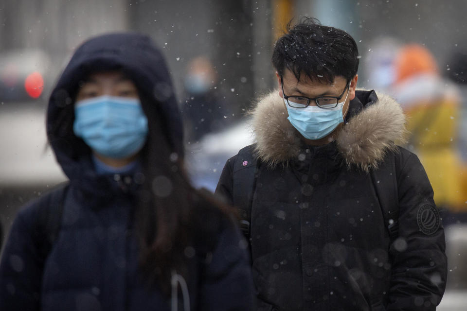 People wearing face masks to protect against the spread of the coronavirus walk along a street during a snowy morning in Beijing, Tuesday, Jan. 19, 2021. A Chinese province near Beijing grappling with a spike in coronavirus cases is reinstating tight restrictions on weddings, funerals and other family gatherings, threatening violators with criminal charges. (AP Photo/Mark Schiefelbein)