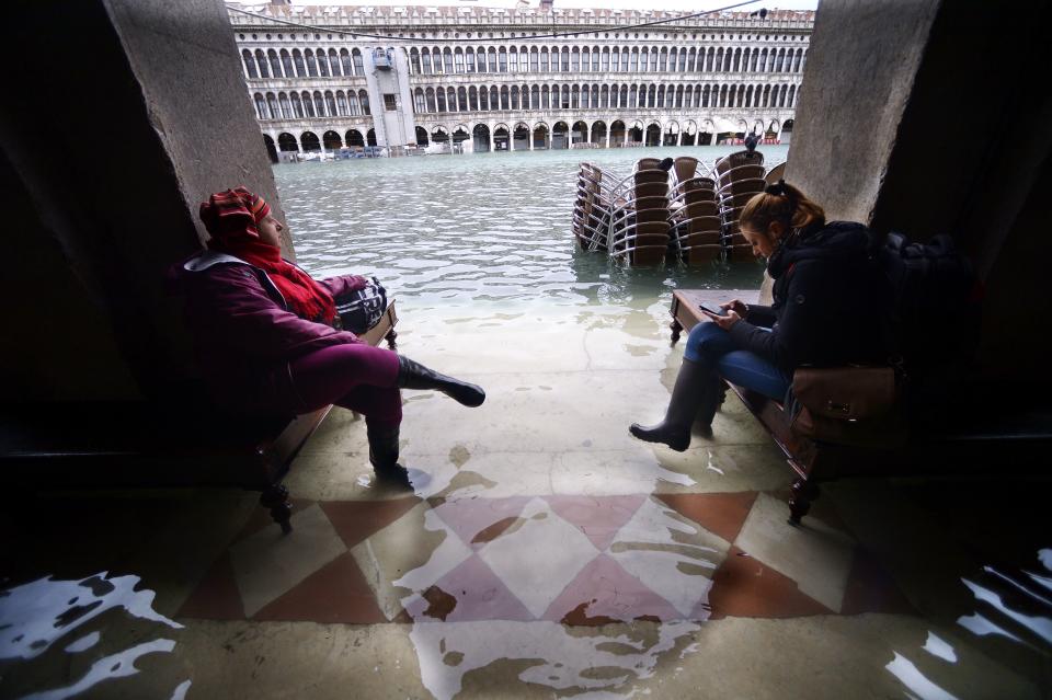 People sit on benches in a flooded arcade by St. Mark's Square on November 15, 2019 in Venice, two days after the city suffered its highest tide in 50 years. - Flood-hit Venice was bracing for another exceptional high tide on November 15, as Italy declared a state of emergency for the UNESCO city where perilous deluges have caused millions of euros worth of damage. (Photo by FILIPPO MONTEFORTE/AFP via Getty Images)