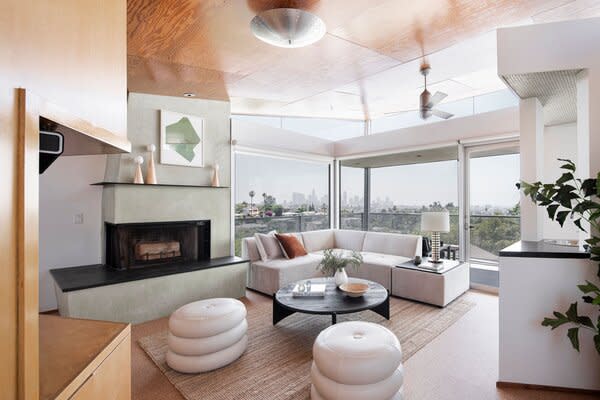 A spacious living room awaits on the upper level, featuring cork flooring, a sage-green fireplace which pops against the wooden ceiling, and walls of glass to frame vast city views.