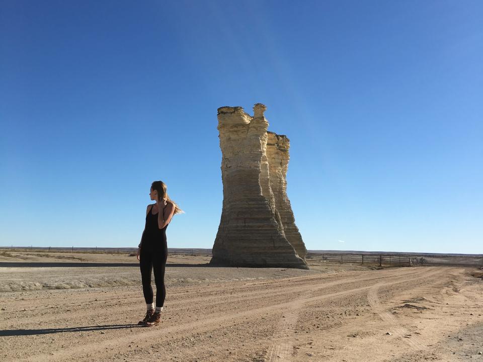 Emily looks out at the barren landscape while standing in from of a giant rock formation.