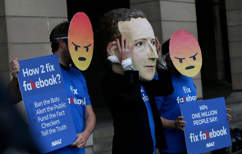 A protester wears a mask with the face of Facebook founder Mark Zuckerberg, in between men wearing angry face emoji masks, during a protest against Facebook outside Portcullis in London on April 26, 2018.