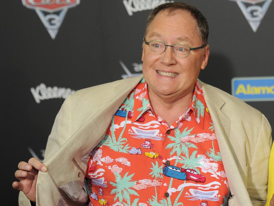 John Lasseter holds open his jacket on a red carpet.