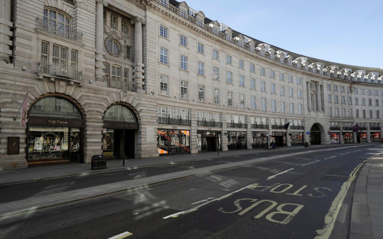 A lone commuter waits at a bus stop in an otherwise deserted Regent Street in London - Matt Dunham/AP