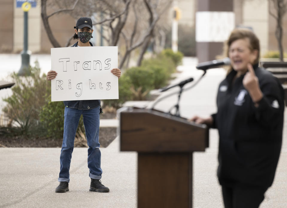 A trans rights activist holds a sign while Idaho state rep. Barbara Erhardt, right, speaks during a rally on Thursday, Jan. 12, 2023, outside of the NCAA Convention in San Antonio. (AP Photo/Darren Abate)