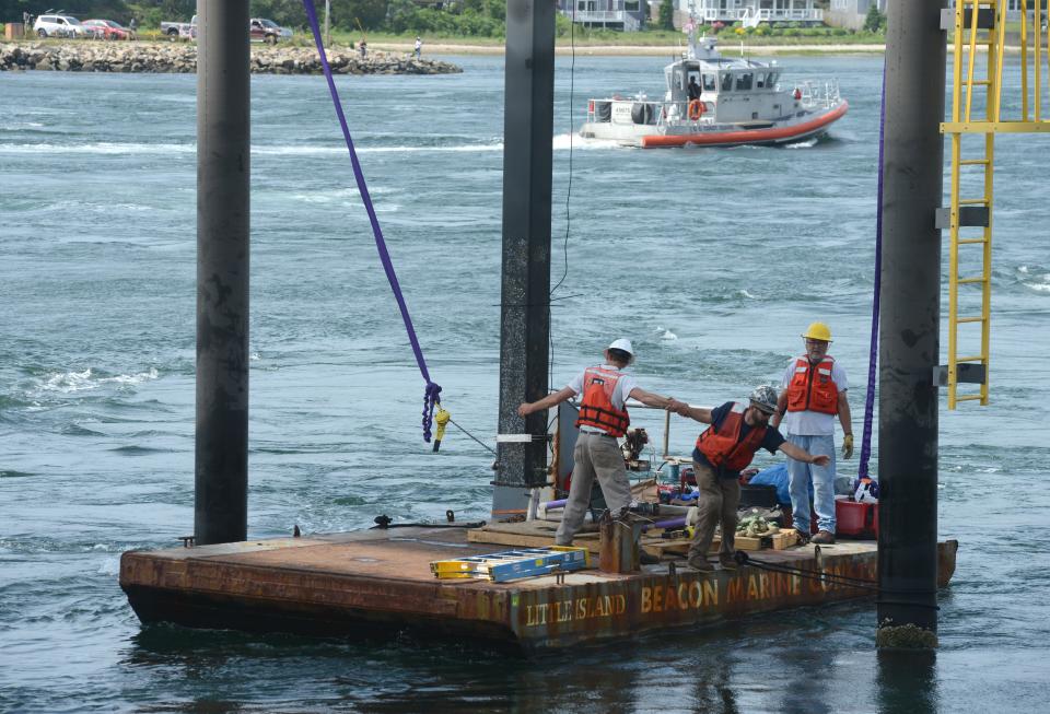 A U.S. Coast Guard boat steams past in 2021 as workers prepare to deploy a tidal turbine onto a lift arm on a platform just west of the railroad bridge on the Cape Cod Canal in Buzzards Bay. The site is used to test technology that would allow tidal waters to produce electric power.