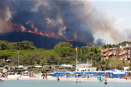 Flames and smoke fill the sky above a burning hillside as tourists swim on the beach in Bormes-les-Mimosas, in the Var department, France, July 26, 2017. REUTERS/Jean-Paul Pelissier