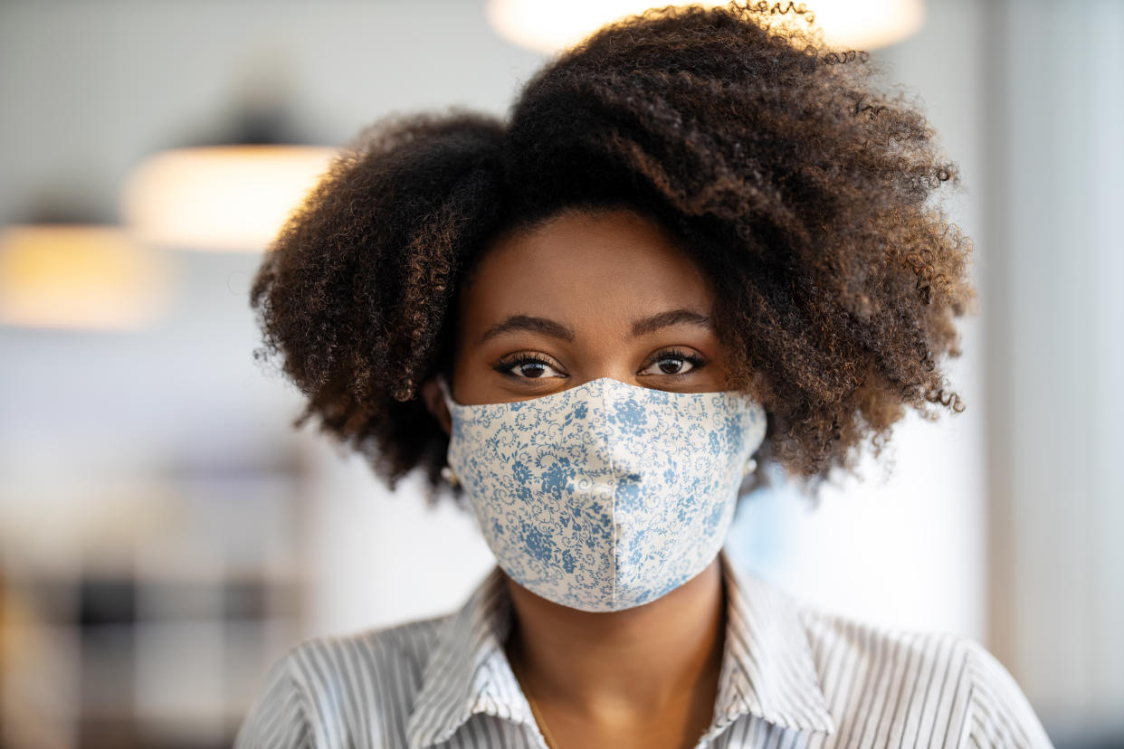 Close-up portrait of an african businesswoman with face mask after returning back to work at office. Woman with protective face mask standing in office and staring at camera.