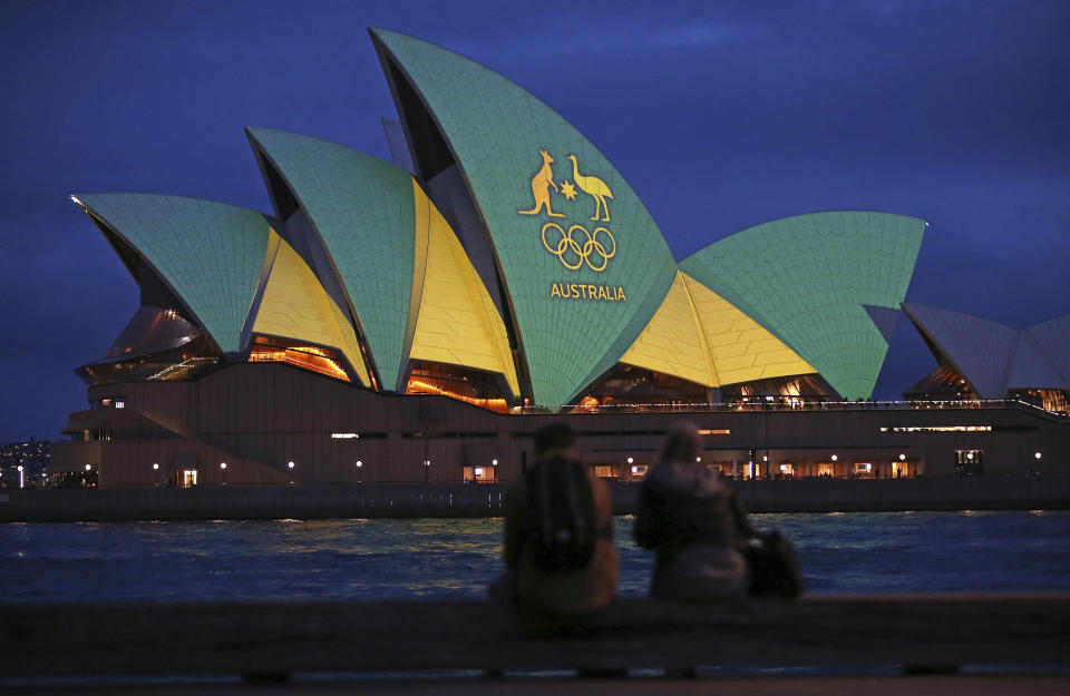 FILE - In this Friday, Aug. 5, 2016, file photo, a couple sit on a dock to look at the sails of the Sydney Opera House that are illuminated with the green and gold colors of the Australian Olympic team. An Australian push to host the 2032 Olympics was elevated overnight to the status of preferred bid, and the people of Brisbane and southeast Queensland state woke up to the news Thursday, Feb. 25, 2021. (AP Photo/Rick Rycroft, File)