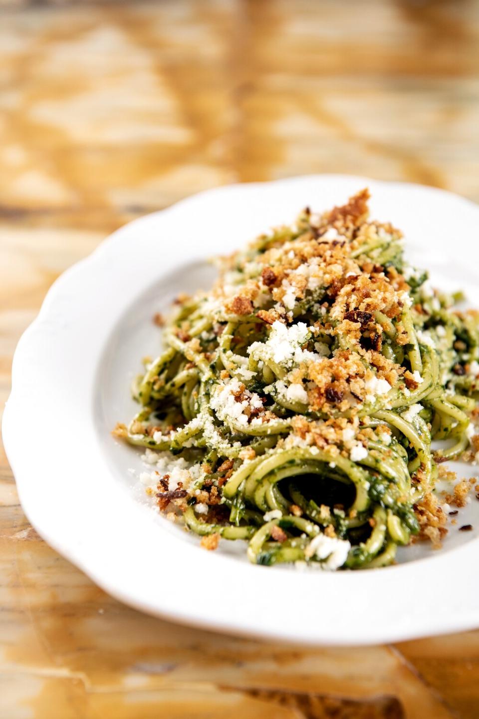 A bowl of green pasta topped with cheese and bread crumbs.