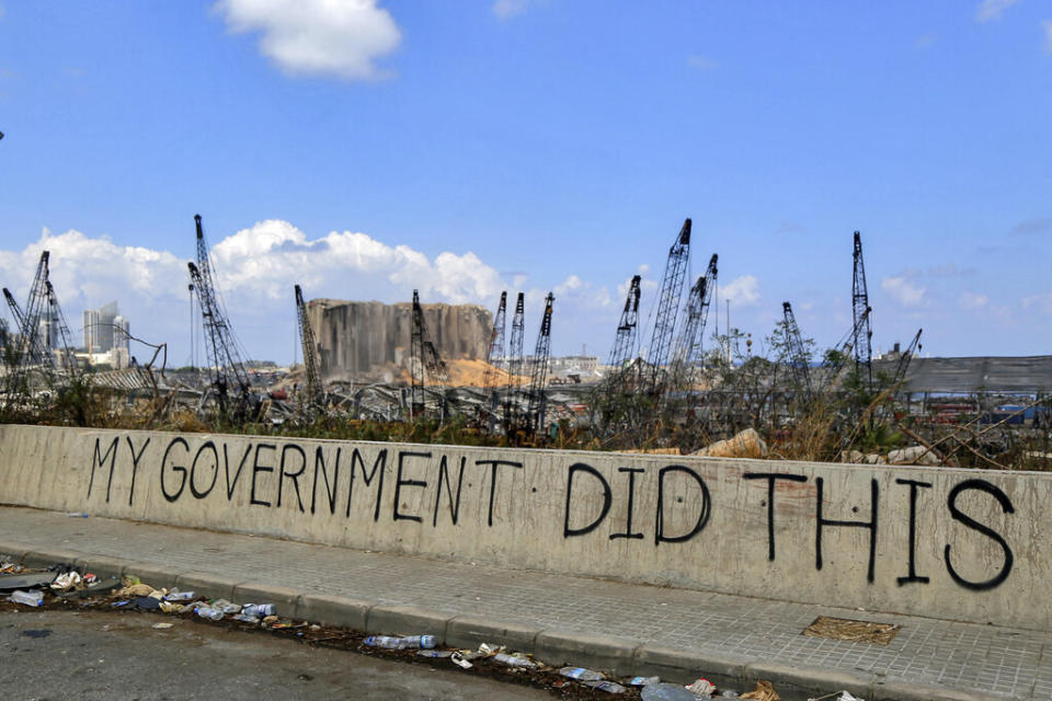 A graffitied barricade reads 'my government did this' in front of miles of desolation and trash