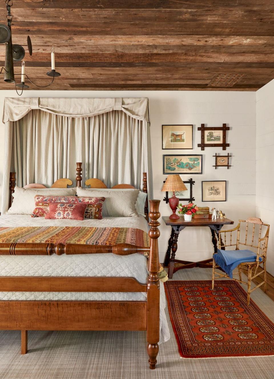 a fancy farmhouse bedroom has a handmade wooden bed with a red rug on the right side and a collection of dog artwork above the bedside table