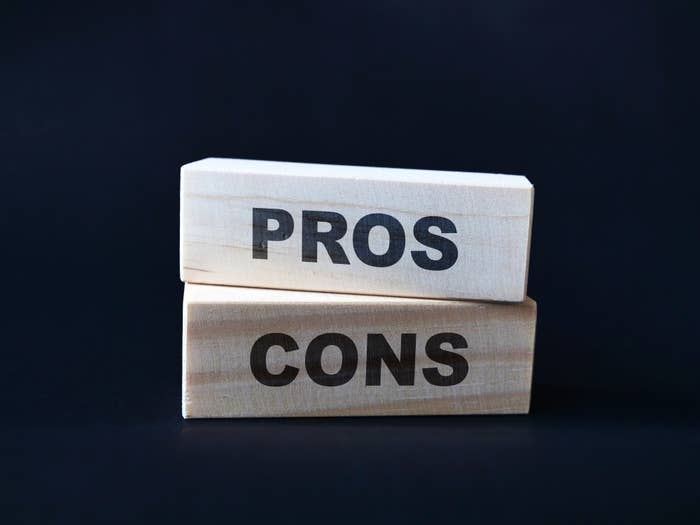 Two wooden blocks stacked; the top block reads "PROS" and the bottom reads "CONS"